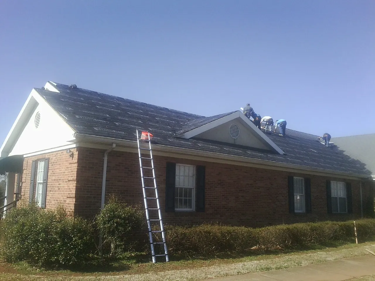 Crew tearing shingles off a brick ranch roof with a ladder set — Emergency Roof Repair work by our crew in Fayette